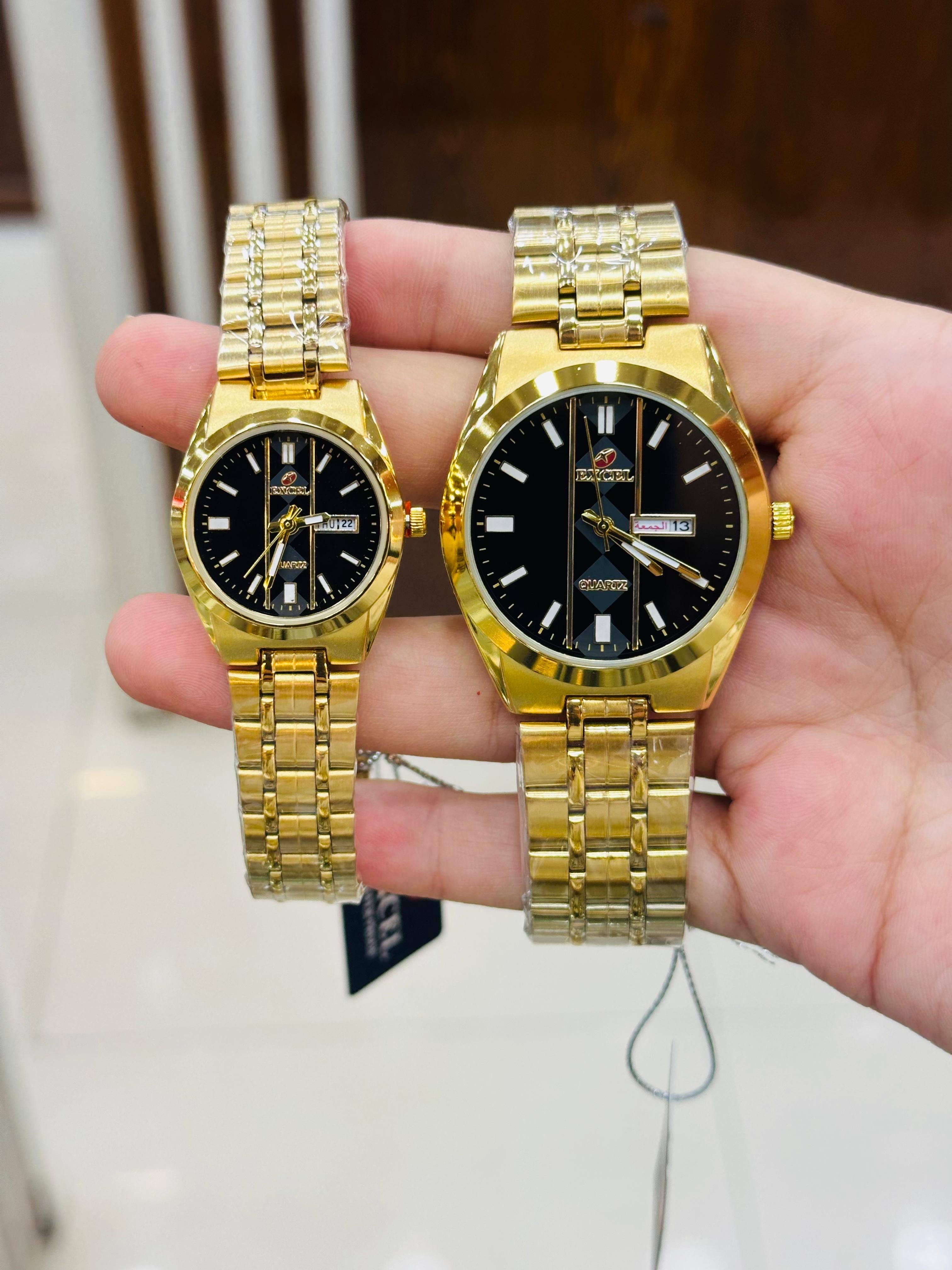 Excel brand quartz watches, a men's and a women's model, both featuring gold-tone stainless steel bands and black dials.